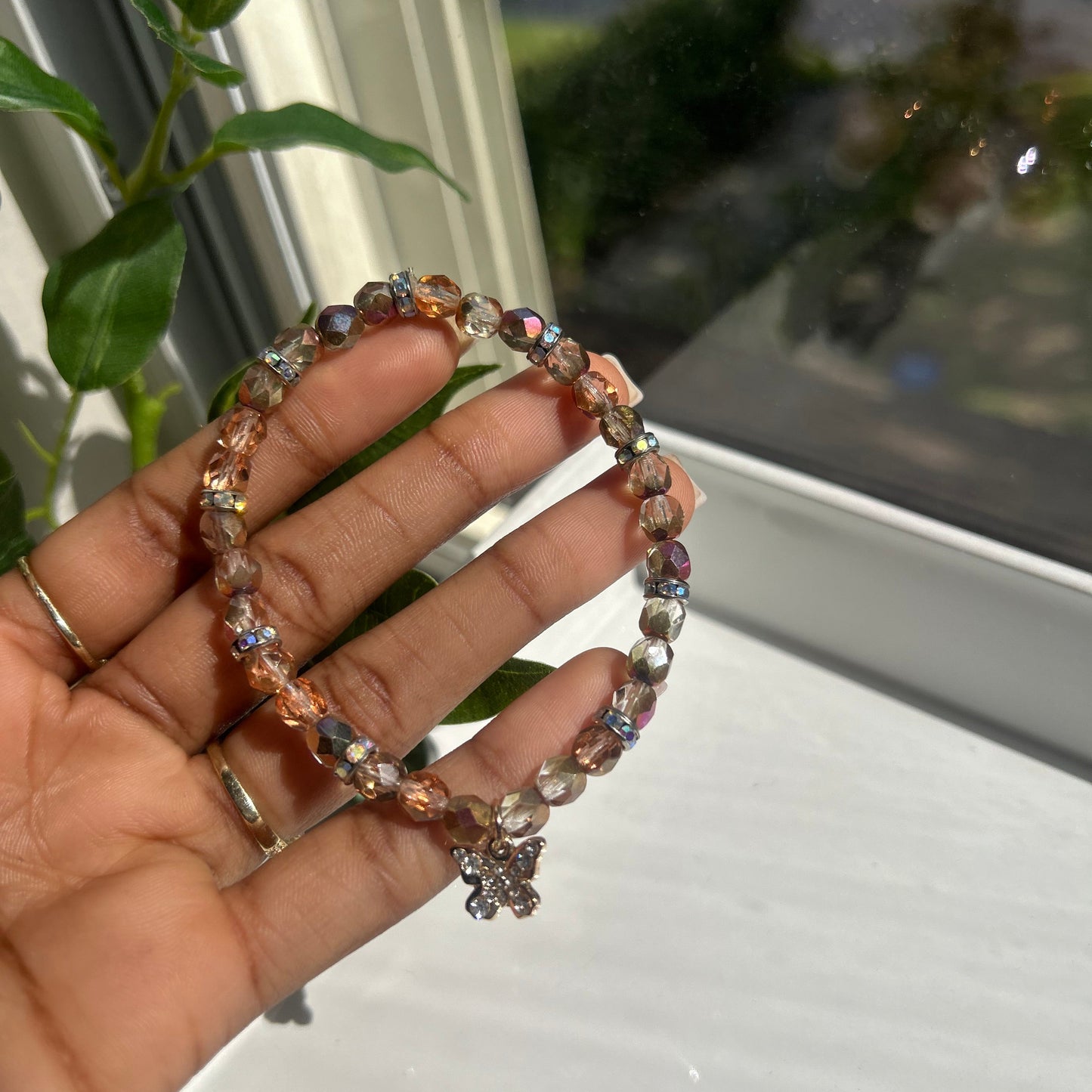 A beaded stretch bracelet with faceted rose gold and iridescent beads, held in a person's hand near a window.