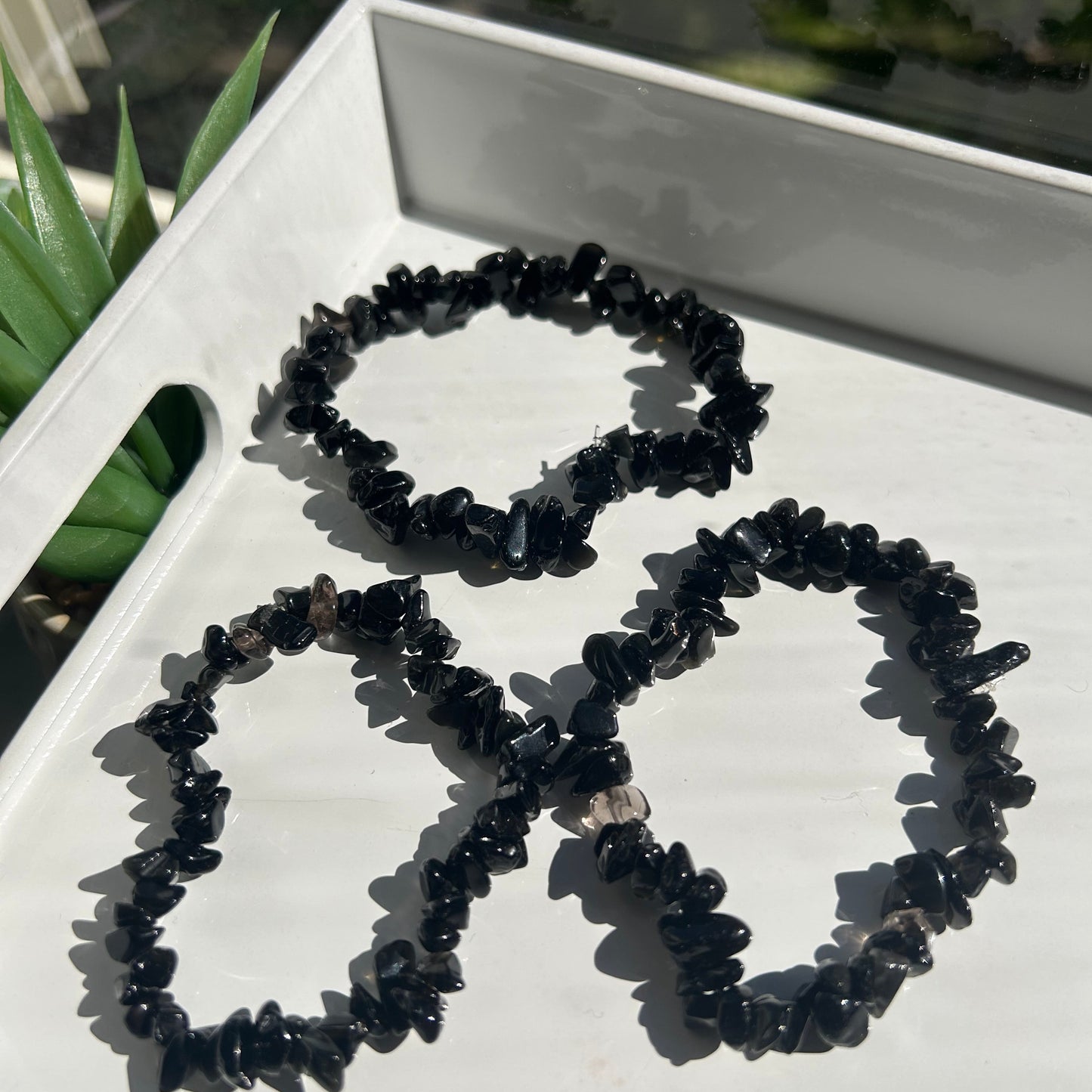 Black beaded necklace on a white stand with blurred greenery in the background