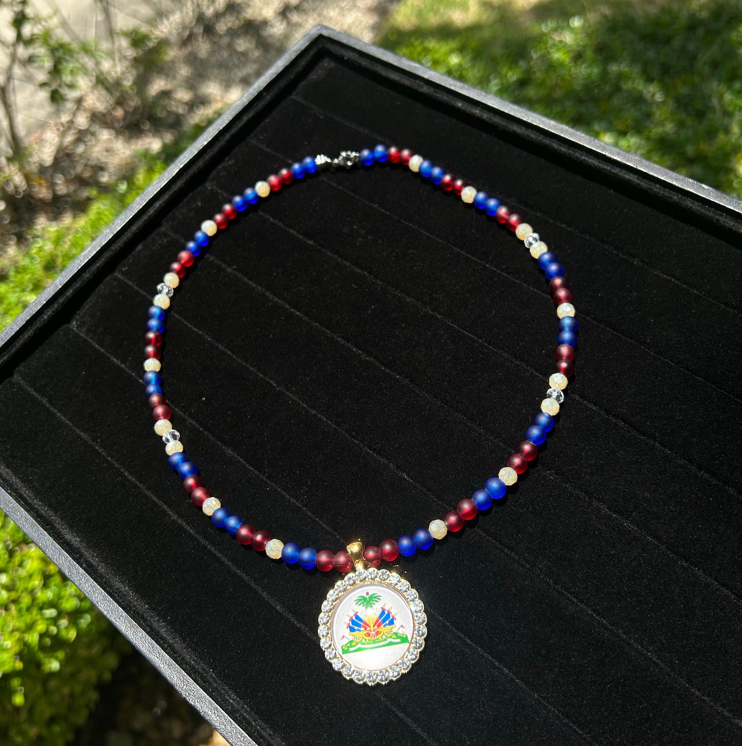 Necklace with colorful beads and a decorative pendant on a black display box outdoors.