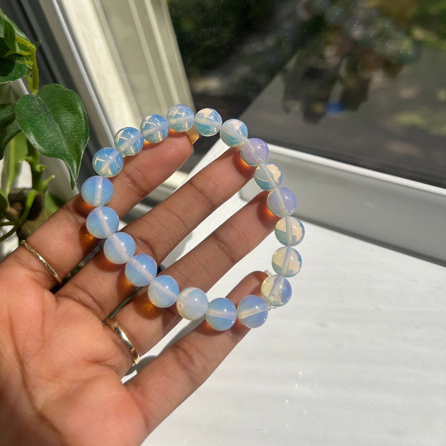 A beaded stretch bracelet made of round, milky white beads with soft blue iridescent highlights, held in a person's hand near a window.