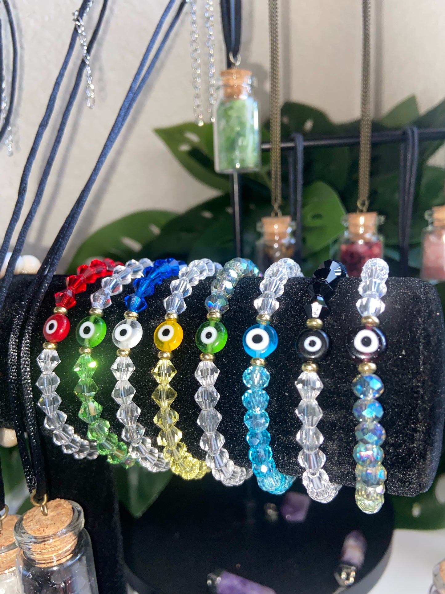 A variety of colorful evil eye gem bracelets displayed on a stand, with different colored beads and a black chain.