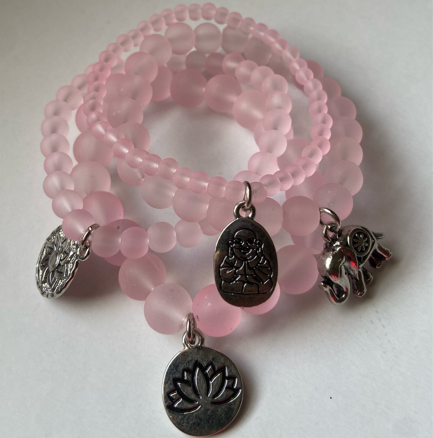 Pink beaded bracelet with silver charms on a white background