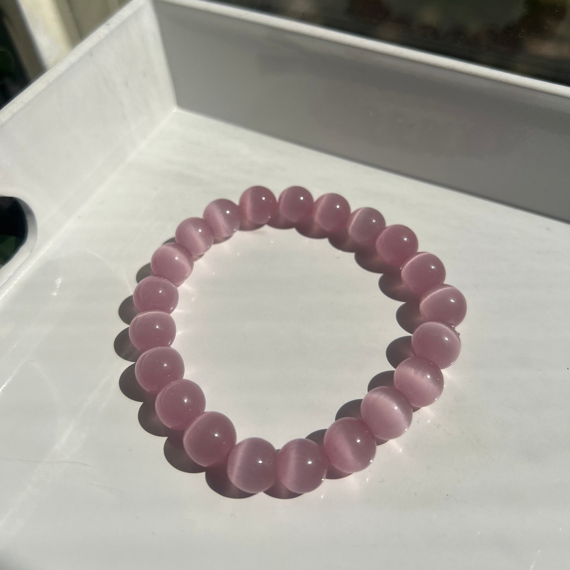 A pink beaded stretch bracelet made of smooth, polished round beads, displayed on a white surface.