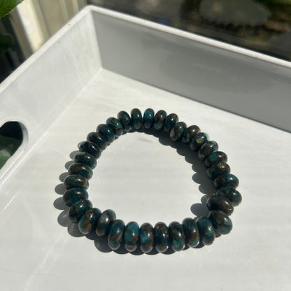 A beaded stretch bracelet made of dark, polished oval beads with a deep teal-blue and black marbled pattern, resting on a white surface.