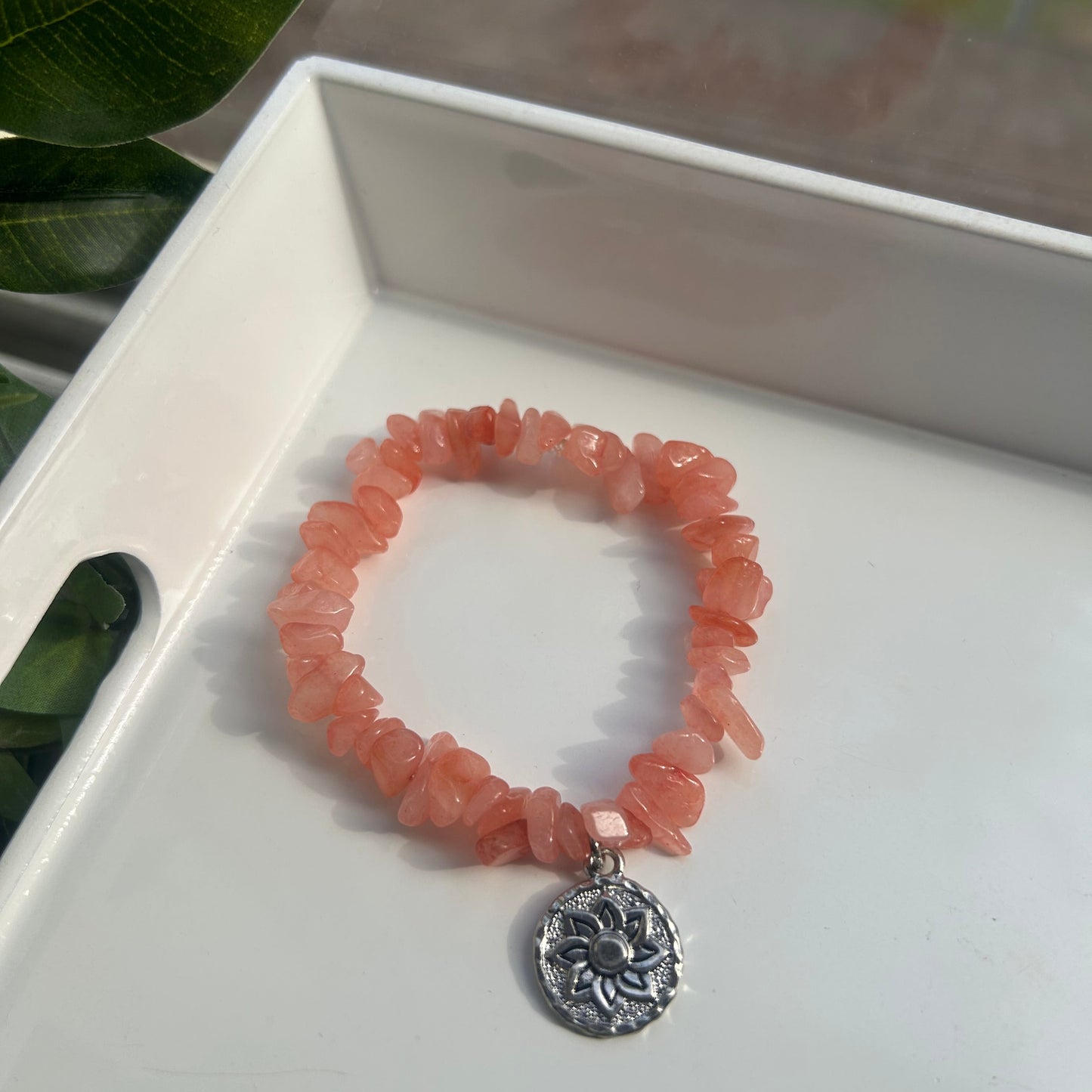 A peach-orange chunky stone bracelet with a silver-toned circular medallion charm, displayed on a white tray.