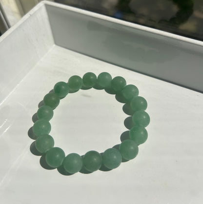 A beaded stretch bracelet made of matte light green round beads, displayed on a white tray.