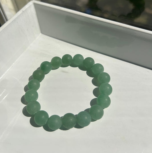 A beaded stretch bracelet made of matte light green round beads, displayed on a white tray.