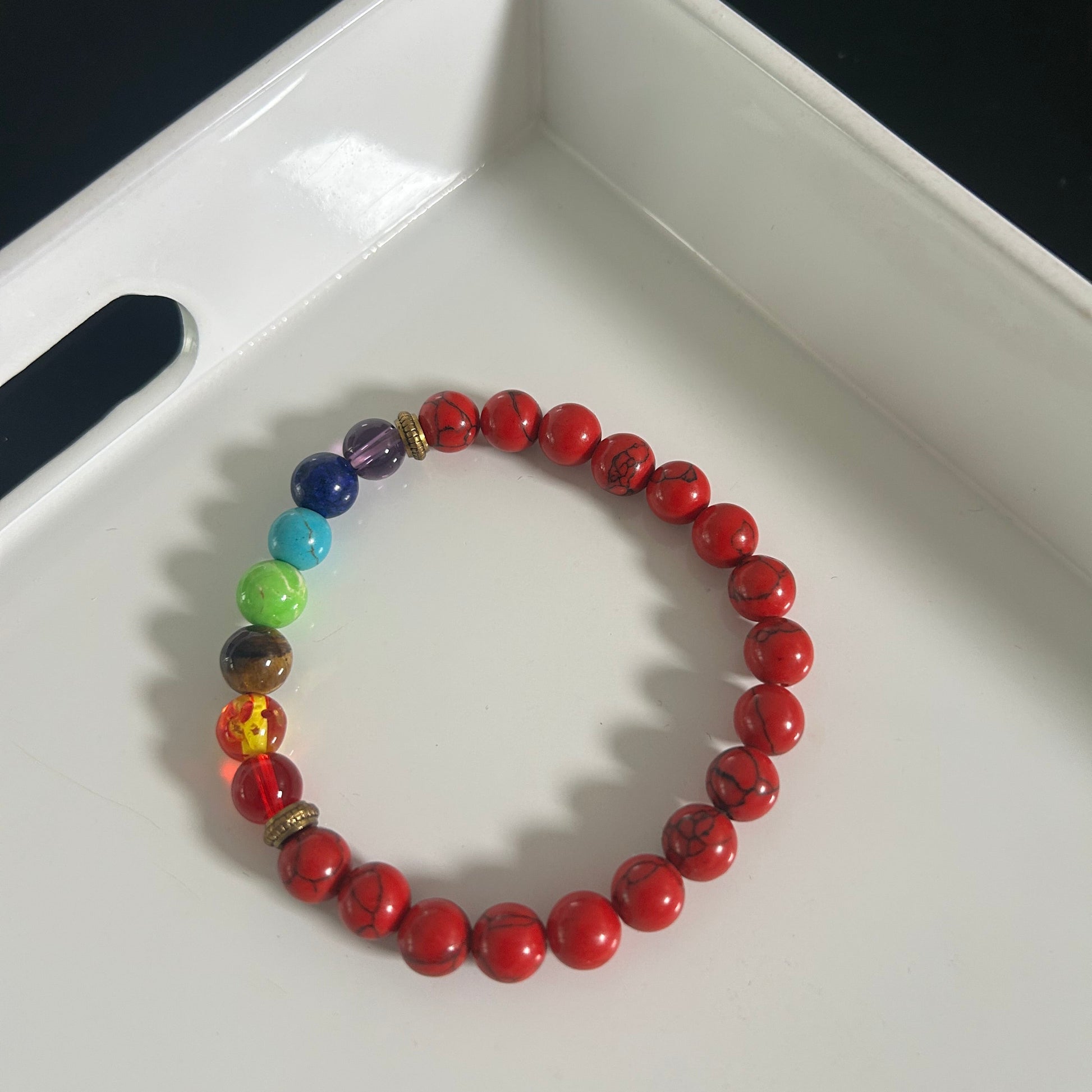 Bracelet with red beads chakra and colorful rainbow beads on a white tray