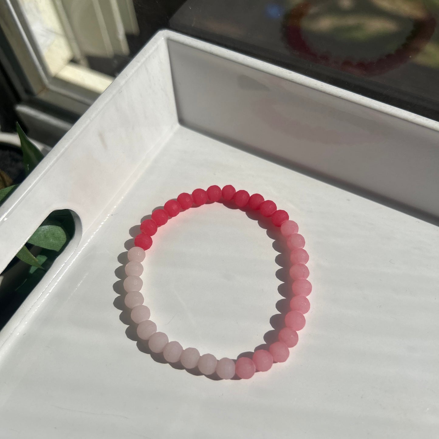 A beaded stretch bracelet with a color gradient from red to light pink and white, displayed on a white tray.