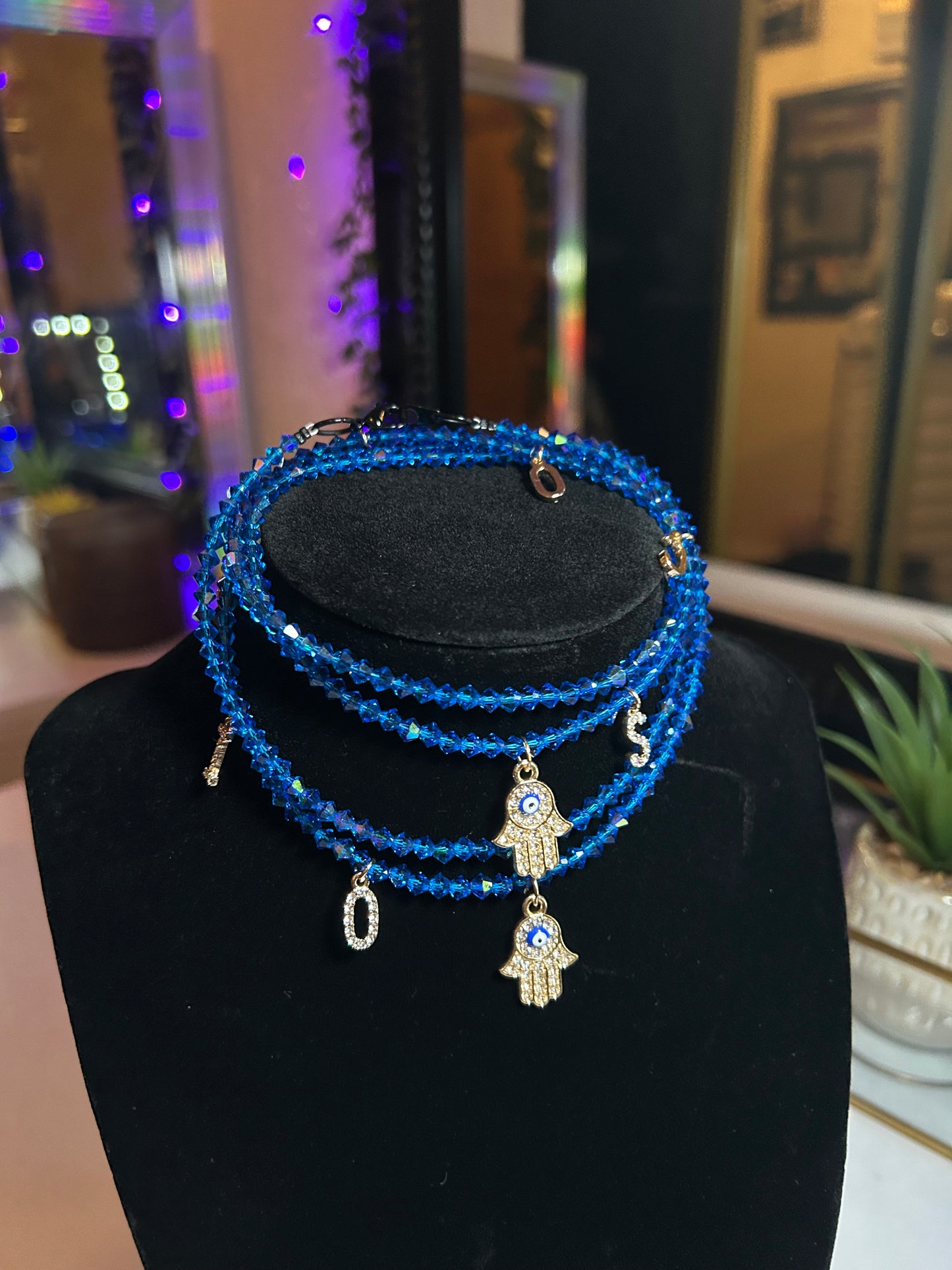 Blue beaded bracelet with a charm on a black stand against a blurred indoor background