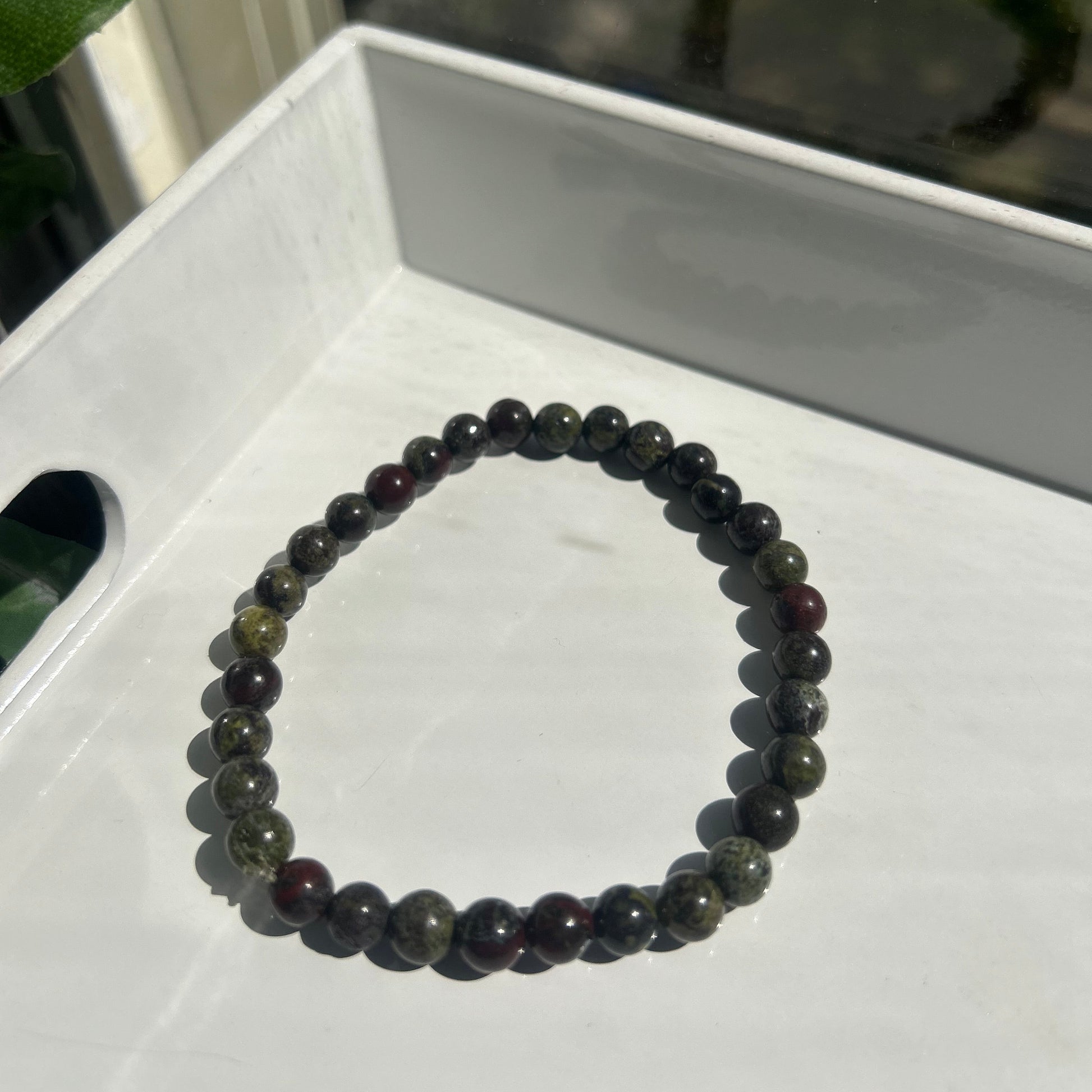 A beaded stretch bracelet made of dark, polished round beads with subtle green and reddish-brown tones, resting on a white tray.