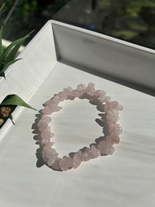 Rose quartz crystal bracelet on a white stand with a blurred natural background