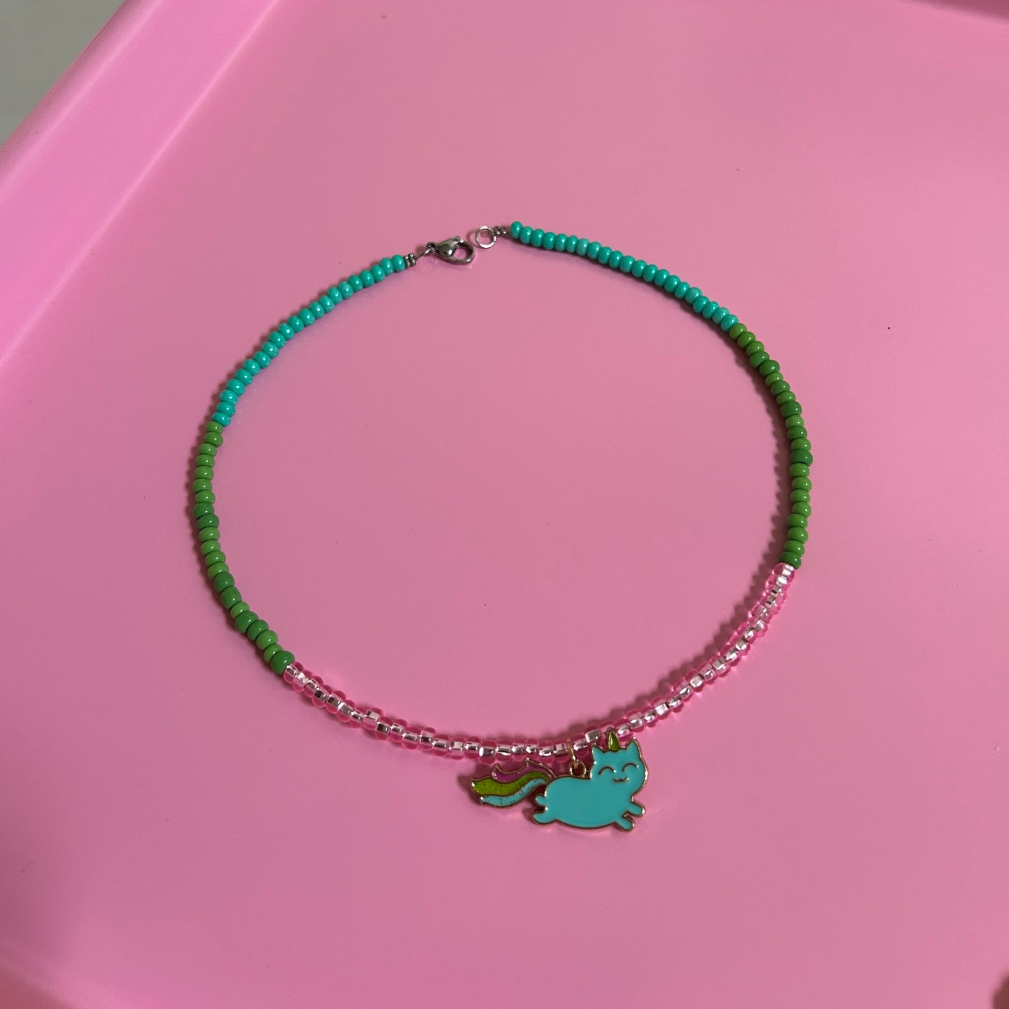 Children Green beaded necklace with a charm on a pink surface