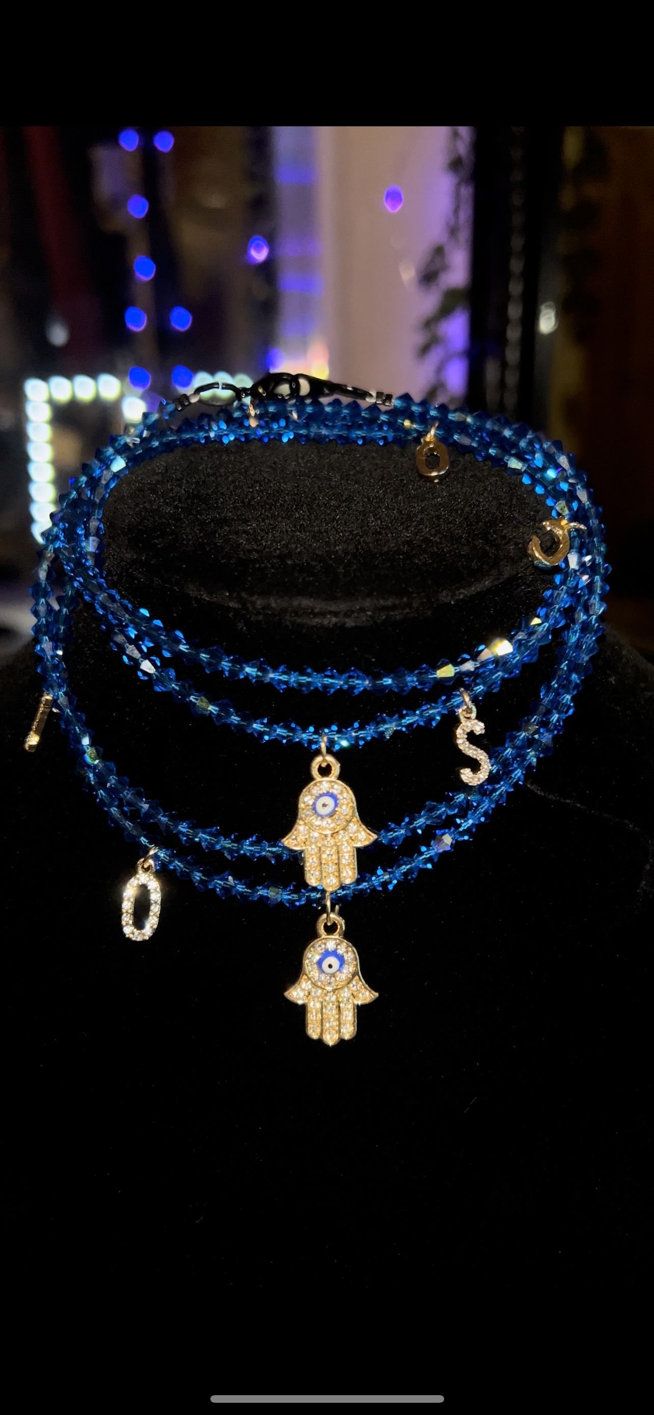 Blue beaded bracelet with gold charms on a black stand against a blurred background