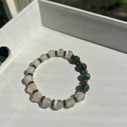 A beaded stretch bracelet with white translucent round beads, turquoise blue marbled beads, and small bronze spacer beads, displayed on a white surface.