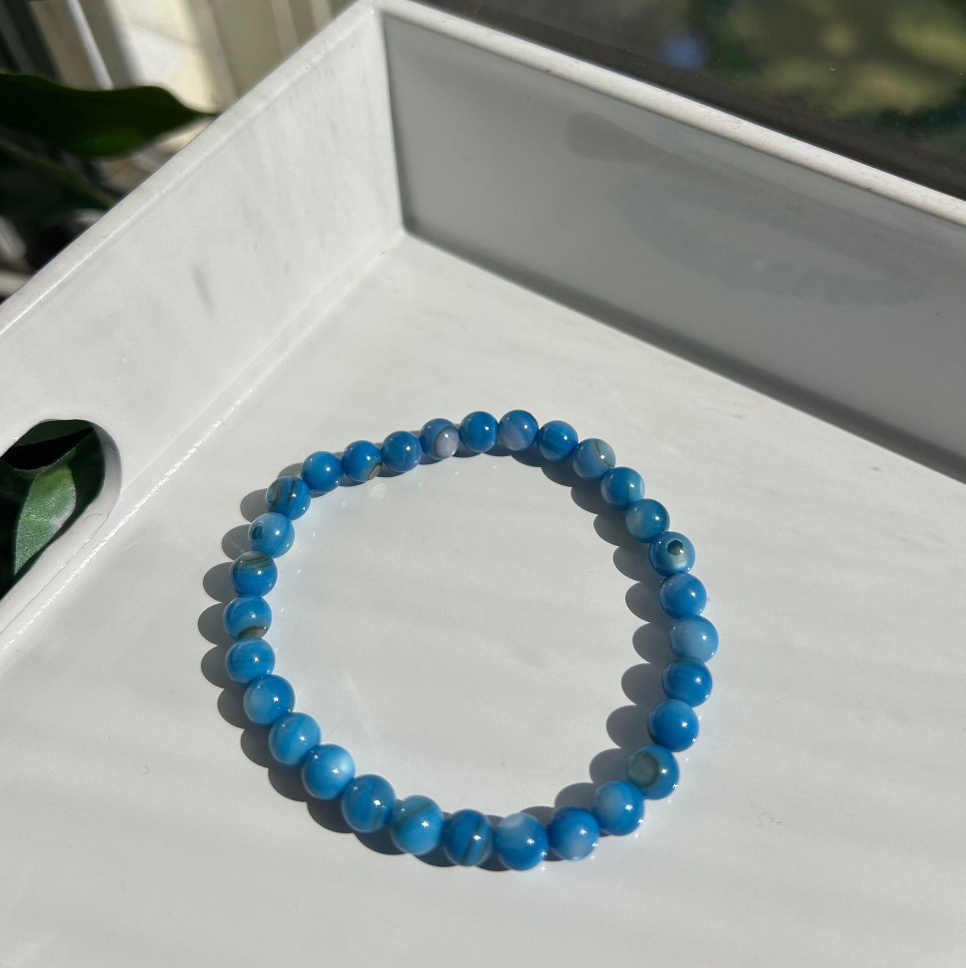 A beaded stretch bracelet made of round blue beads with natural white and gray marbling, resting on a white tray.