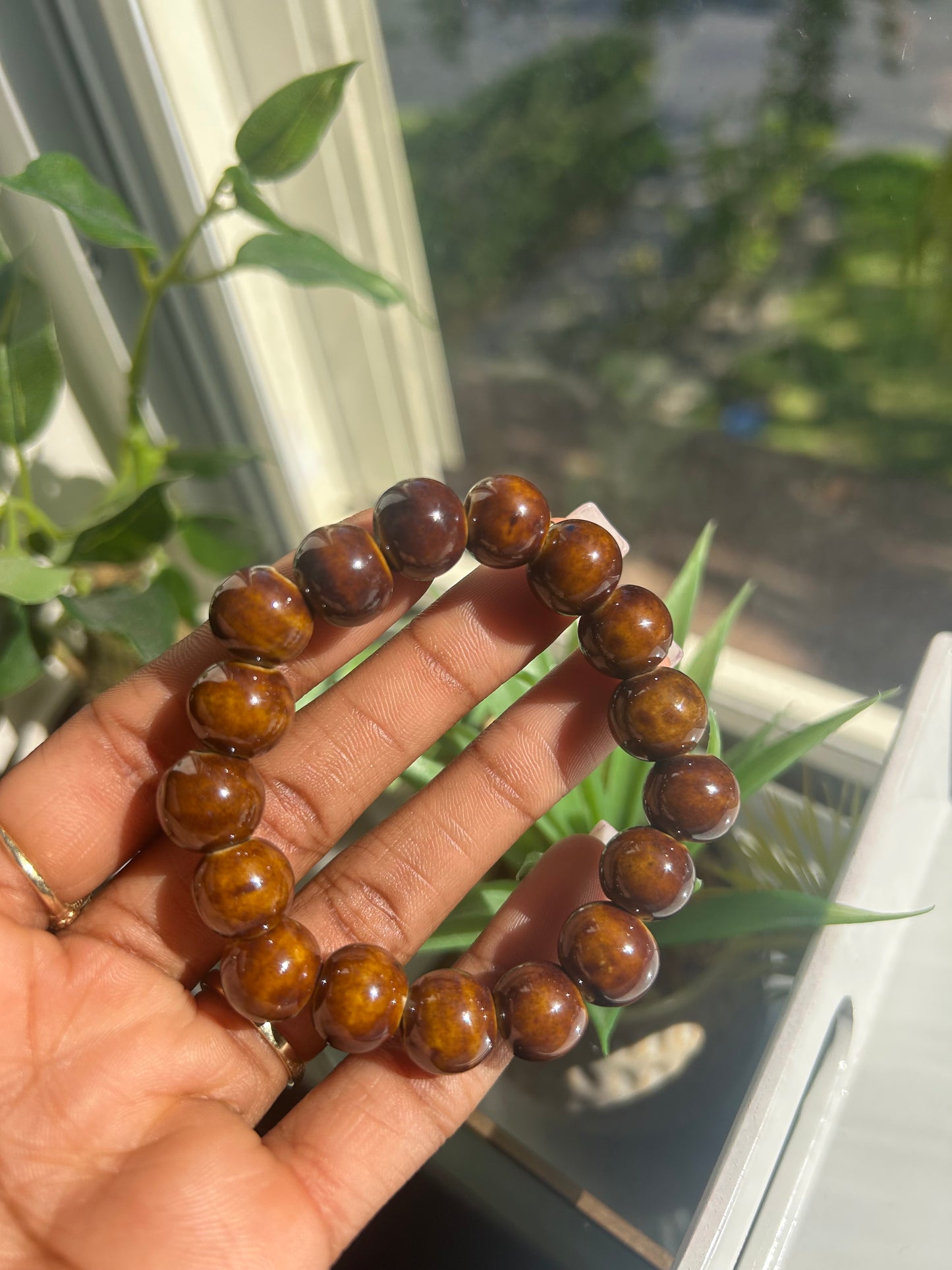 Hand holding a bracelet with brown beads in front of a window with greenery
