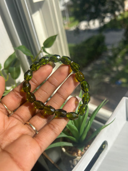 Hand holding a green beaded bracelet with a blurred outdoor background