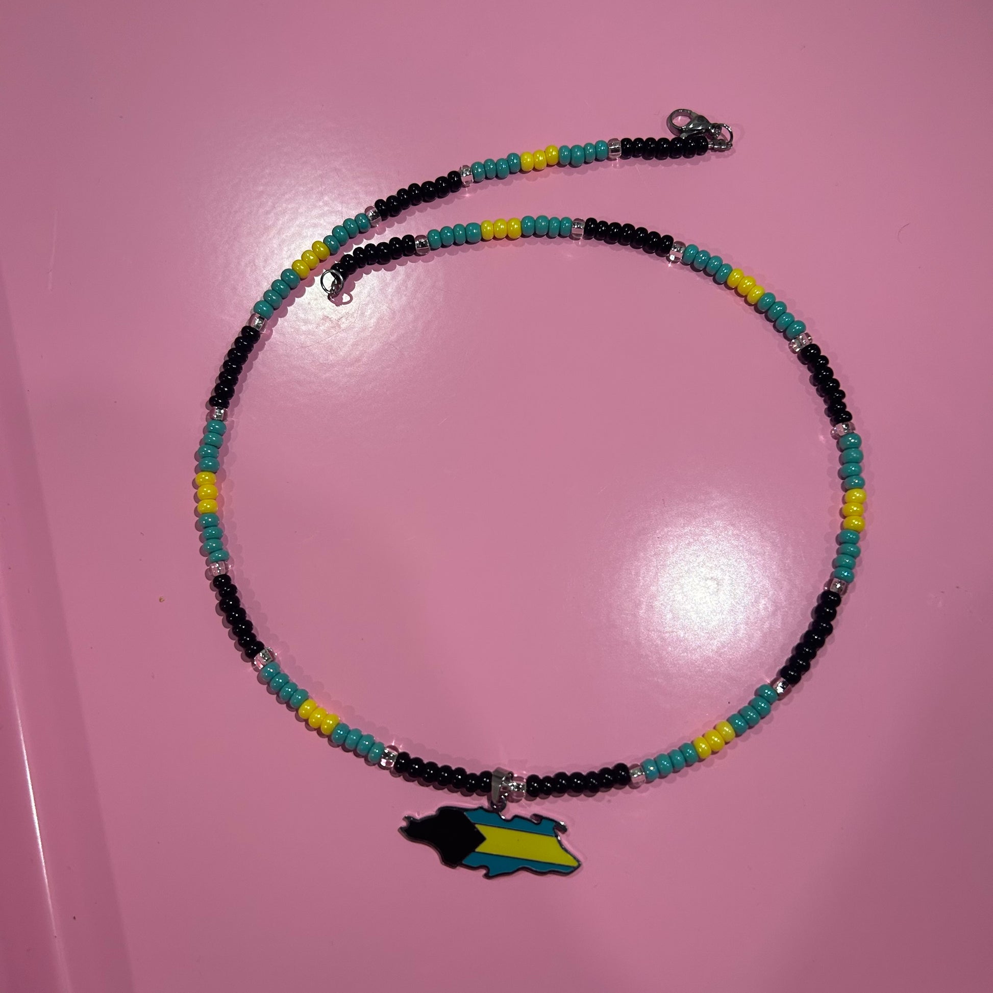 Necklace with colorful beads and a map charm on a pink surface