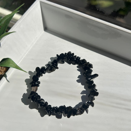 Black beaded bracelet on a white surface with a plant in the background