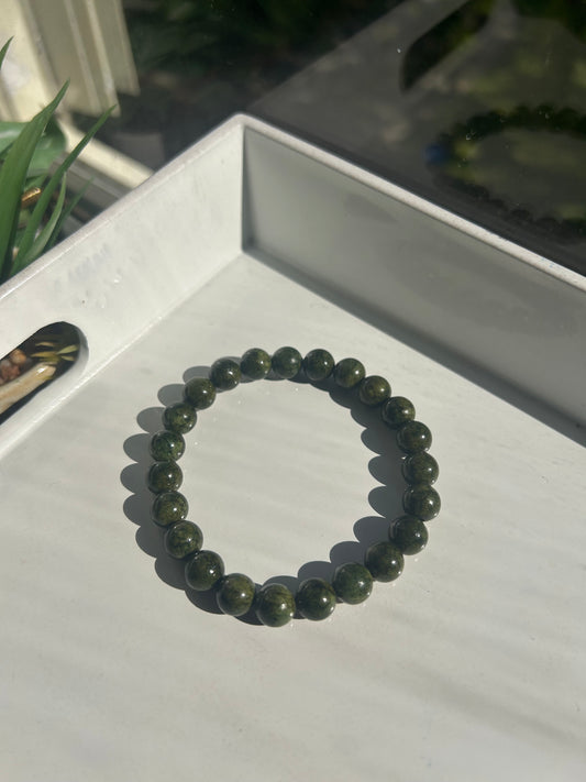 Green beaded bracelet on a white surface with a blurred background