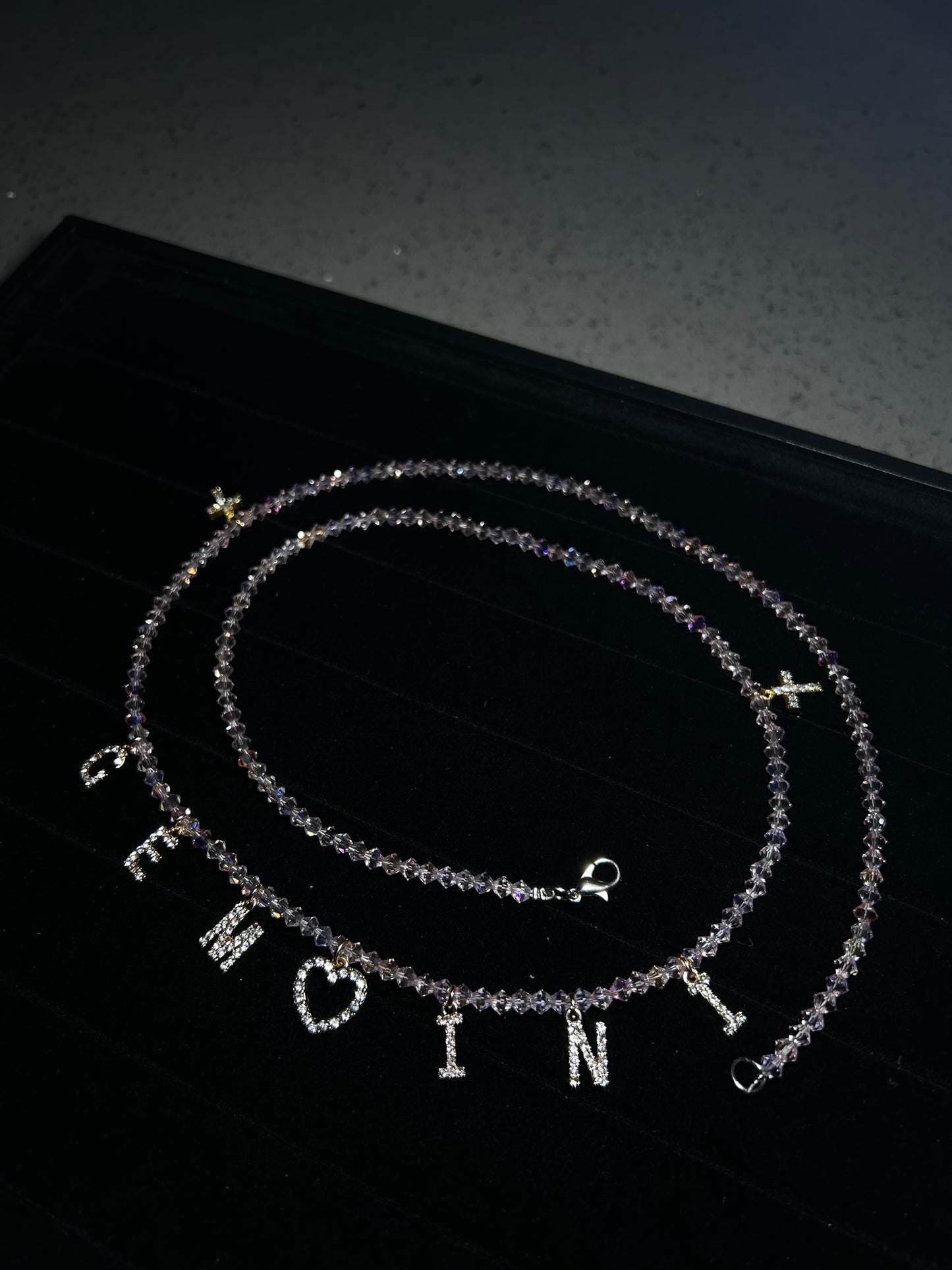 Two silver necklaces with engraved letters on a black background