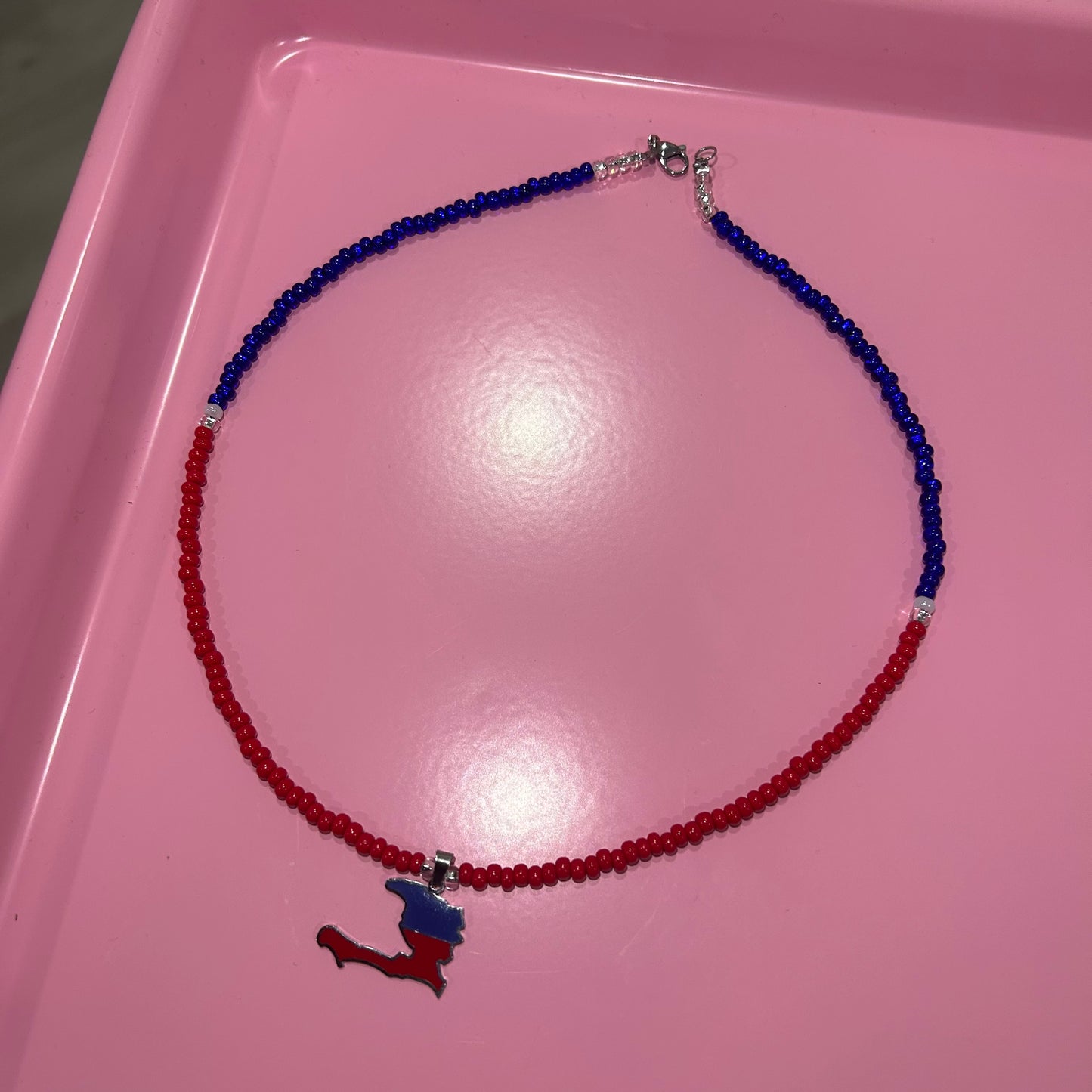 Necklace with red and blue beads and a small figure pendant on a pink surface