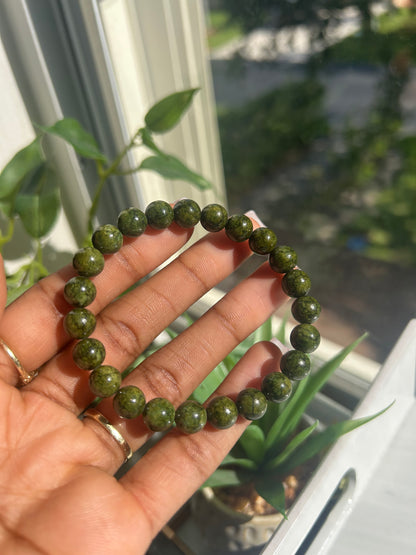 Hand holding a green beaded bracelet with a blurred outdoor background