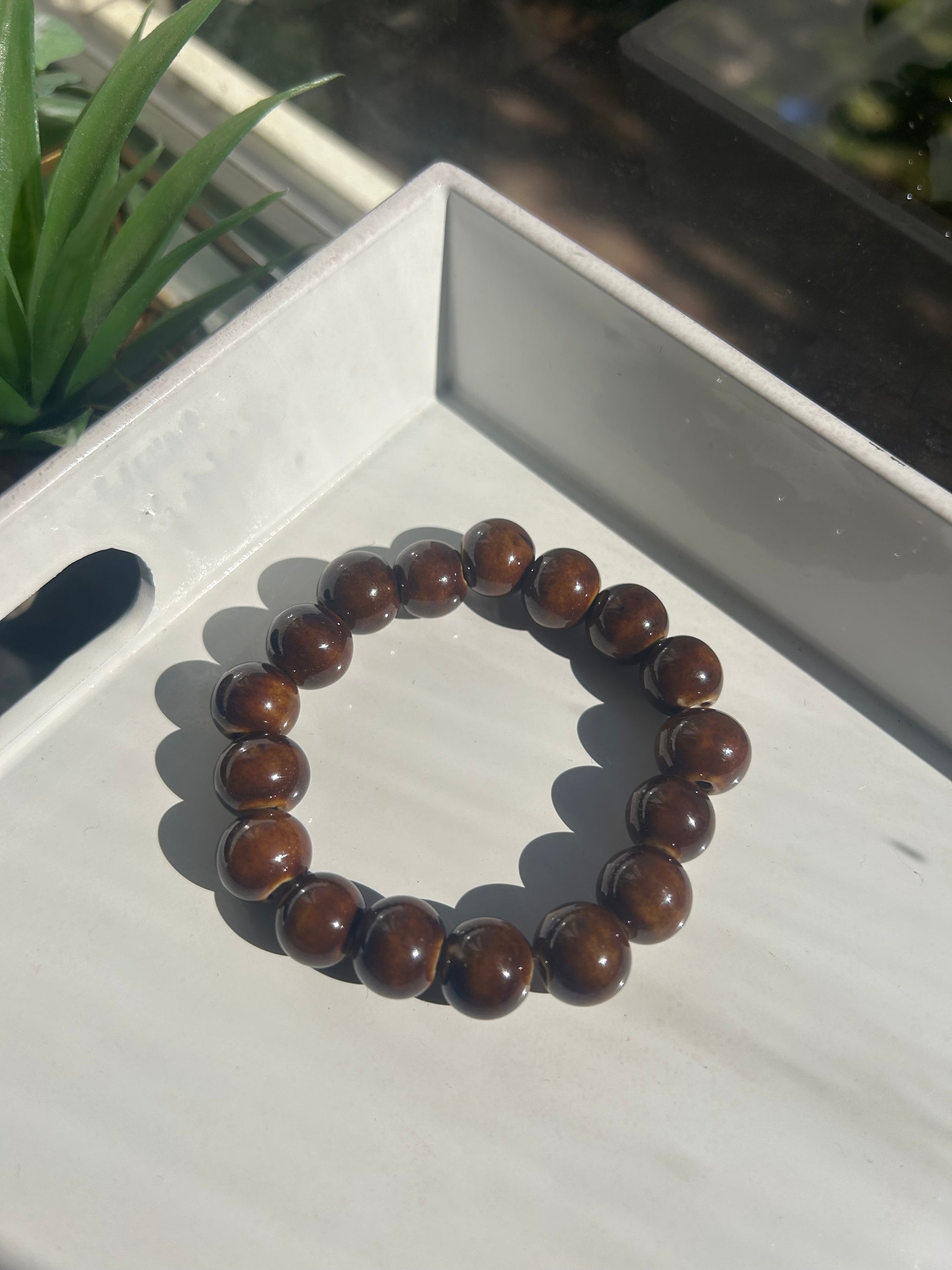Brown beaded bracelet 12MM on a white surface with a plant in the background