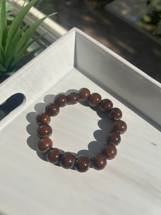 Brown beaded bracelet 12MM on a white surface with a plant in the background