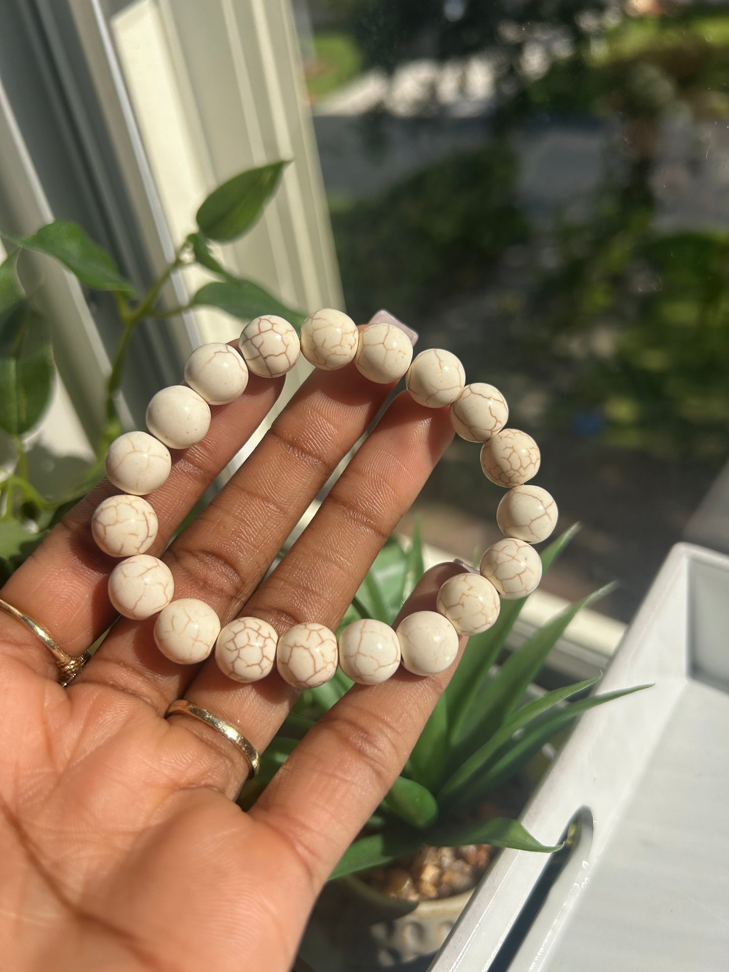 Hand holding a white beaded bracelet with a blurred outdoor background