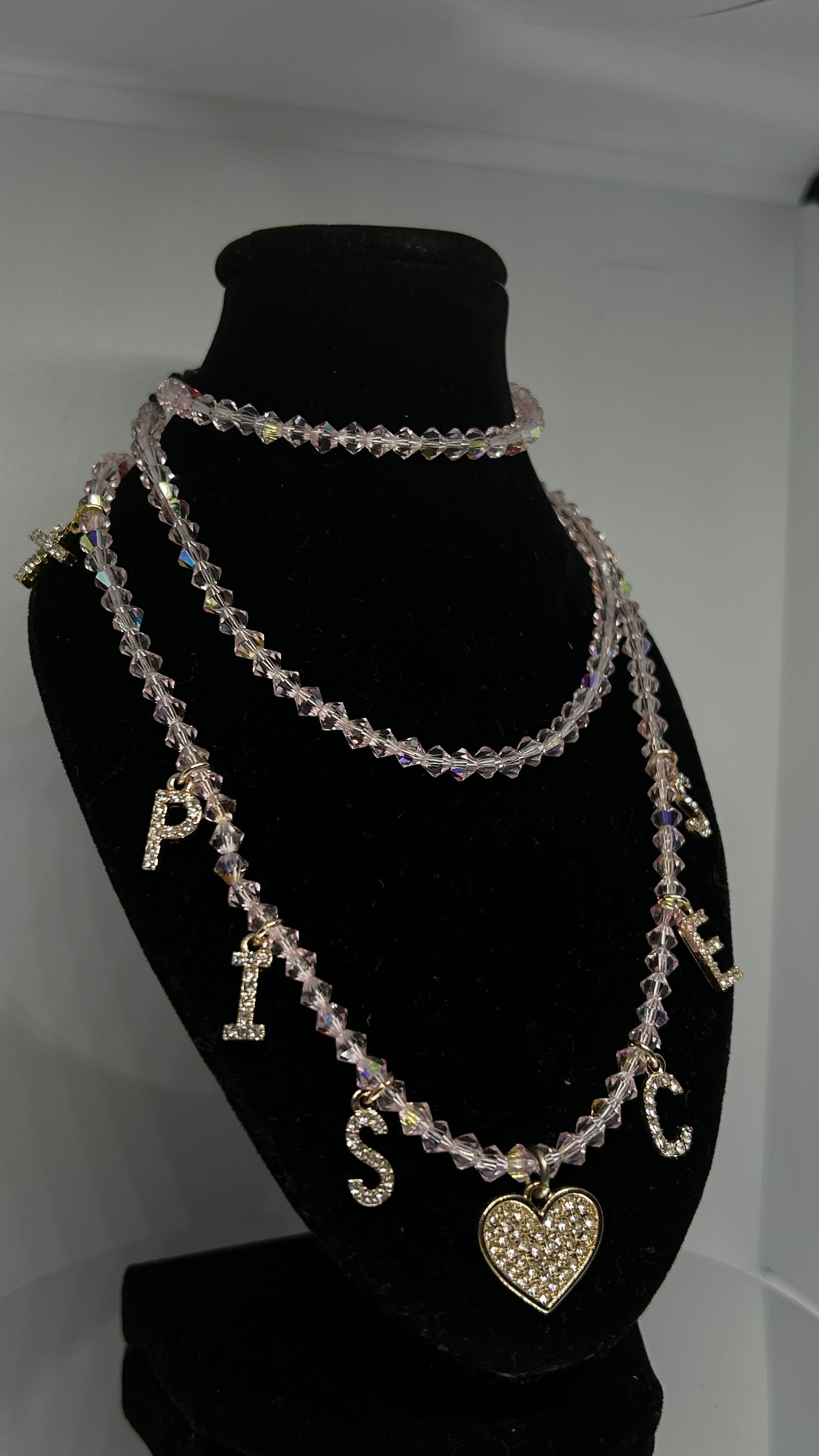Necklace with letter charms on a black mannequin bust against a white background