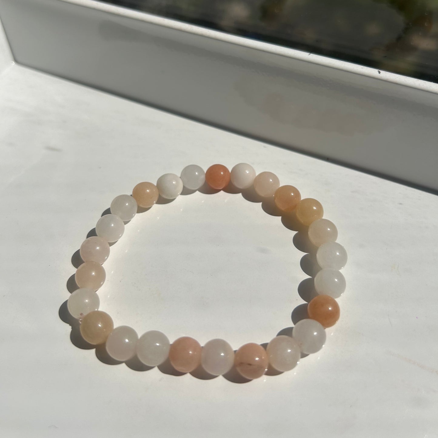 A beaded stretch bracelet made of smooth, translucent round beads in soft peach, cream, and light brown tones, displayed on a white surface.