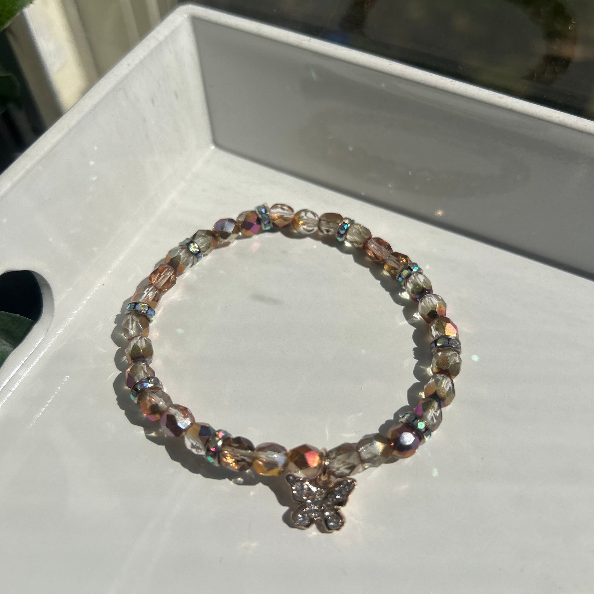 A beaded stretch bracelet with faceted iridescent beads and a small floral clasp, resting on a white tray.