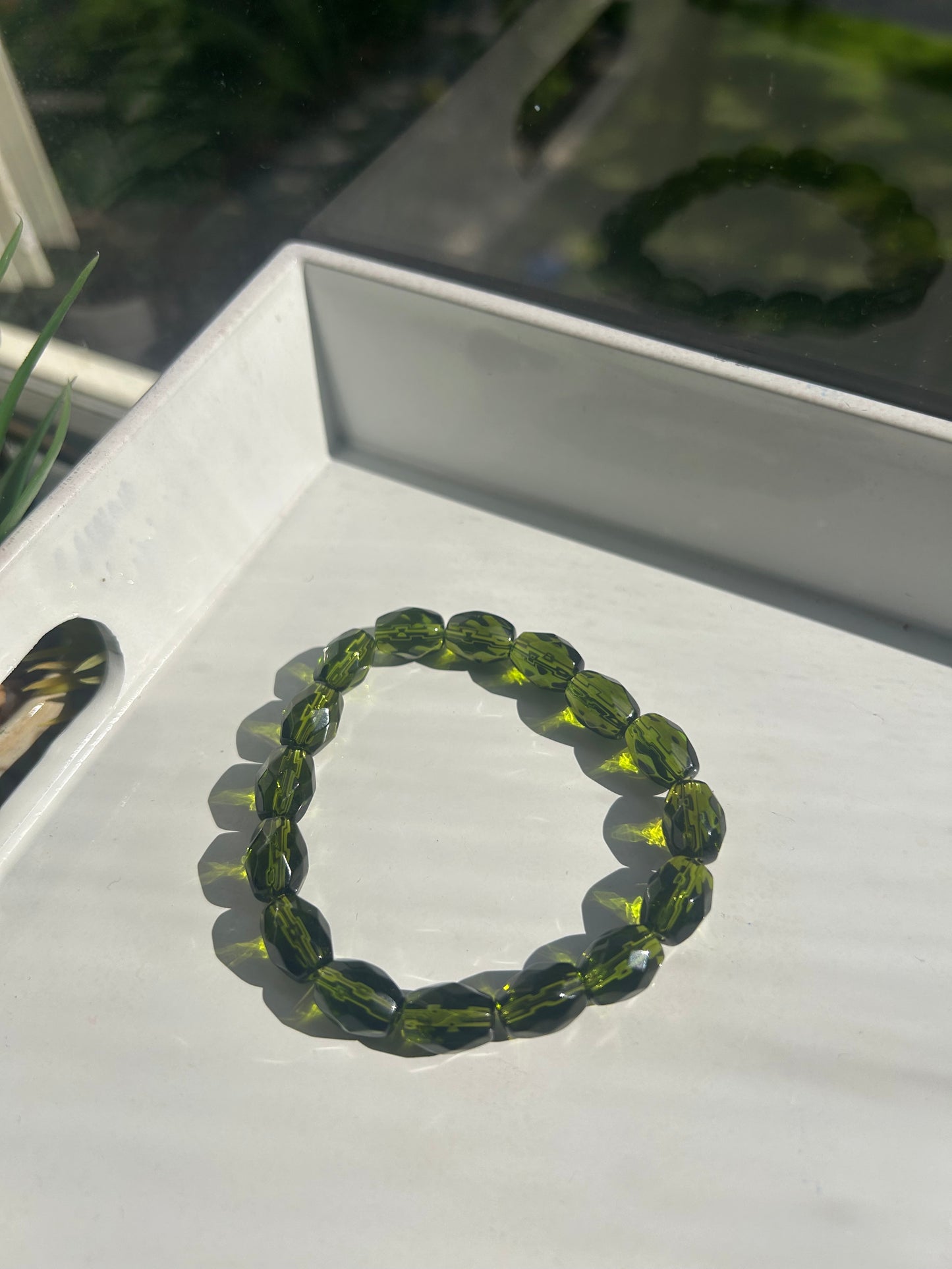 Green beaded bracelet on a white surface with a blurred background