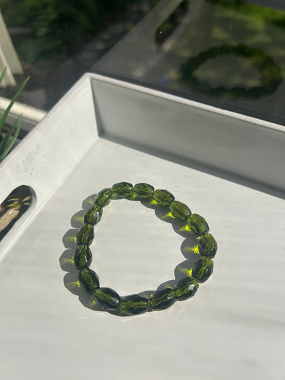 Green beaded bracelet on a white surface with a blurred background