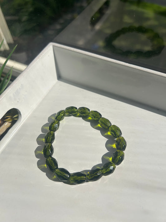 Green beaded bracelet on a white surface with a blurred background