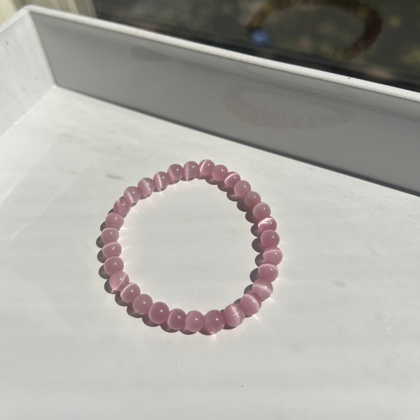 A pink beaded bracelet made of small, polished round beads, displayed on a white surface.