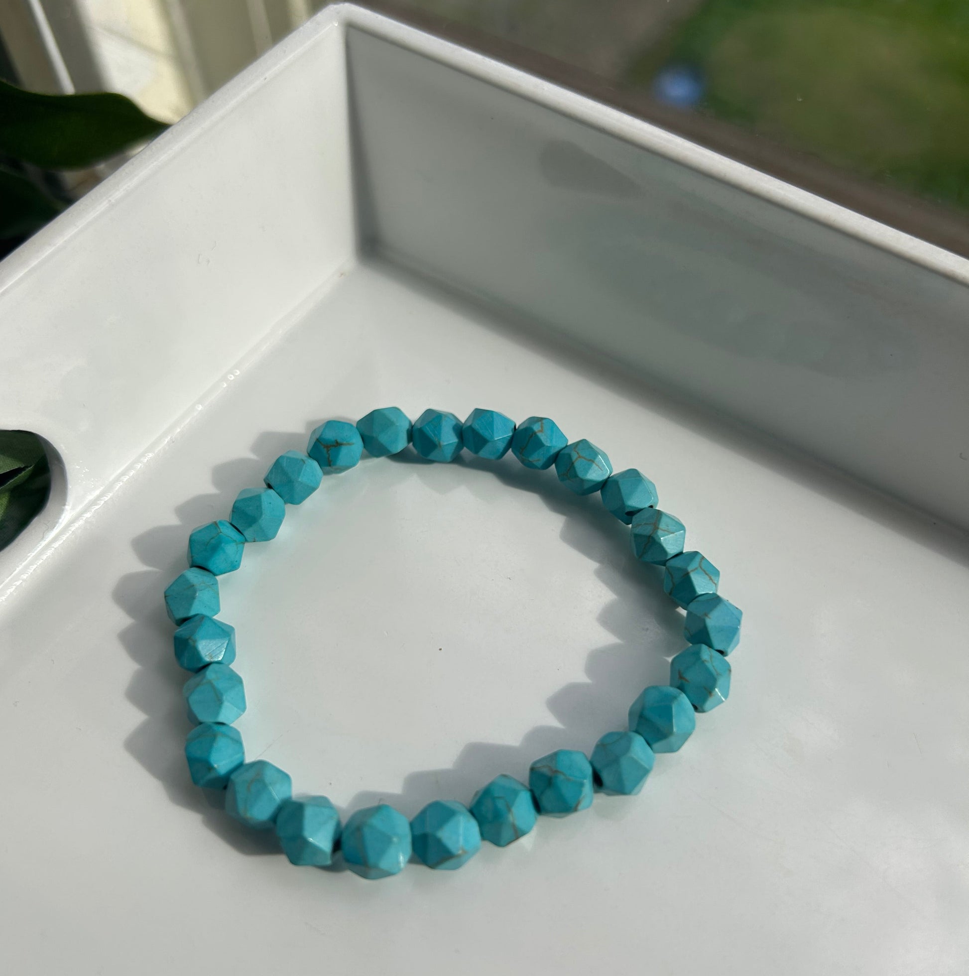A beaded stretch bracelet made of faceted turquoise-blue beads, resting inside a white tray.
