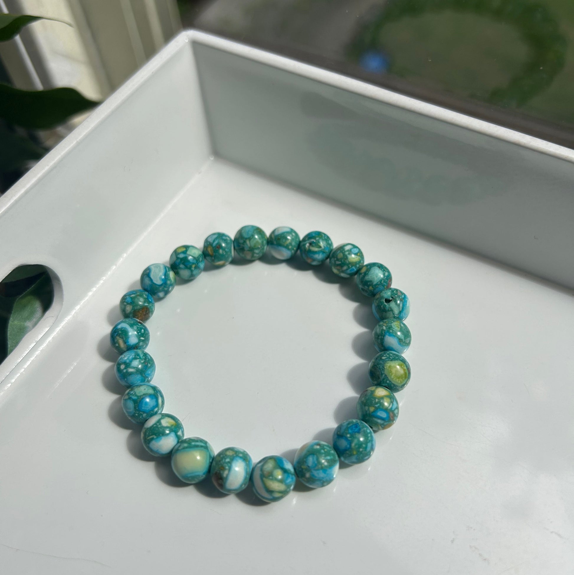 A beaded stretch bracelet made of round turquoise-blue marbled beads with white and green swirls, resting on a white tray.