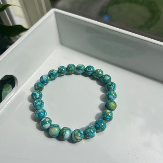 A beaded stretch bracelet made of round turquoise-blue marbled beads with white and green swirls, resting on a white tray.