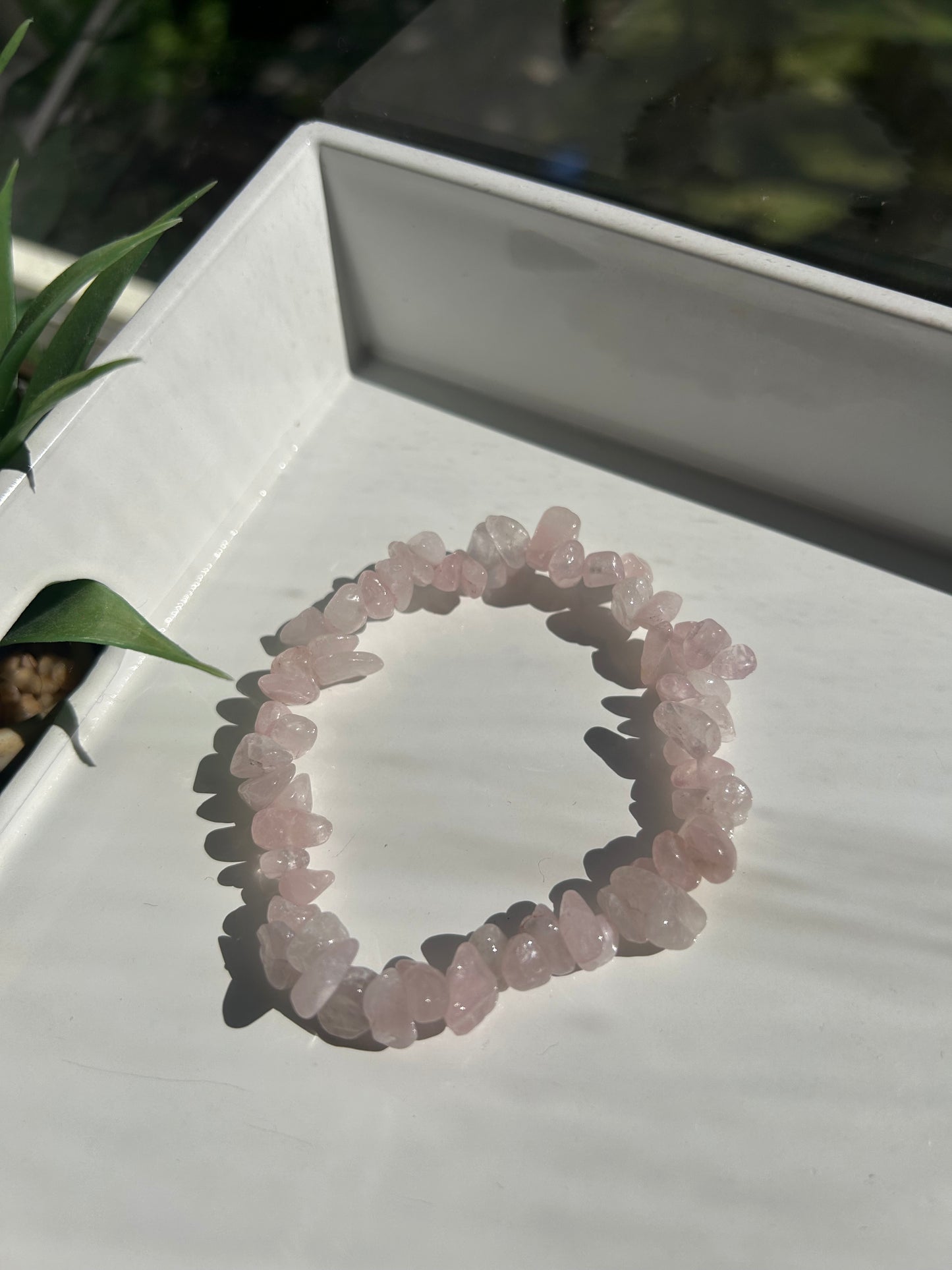 Rose quartz crystal bracelet on a white stand with a blurred natural background