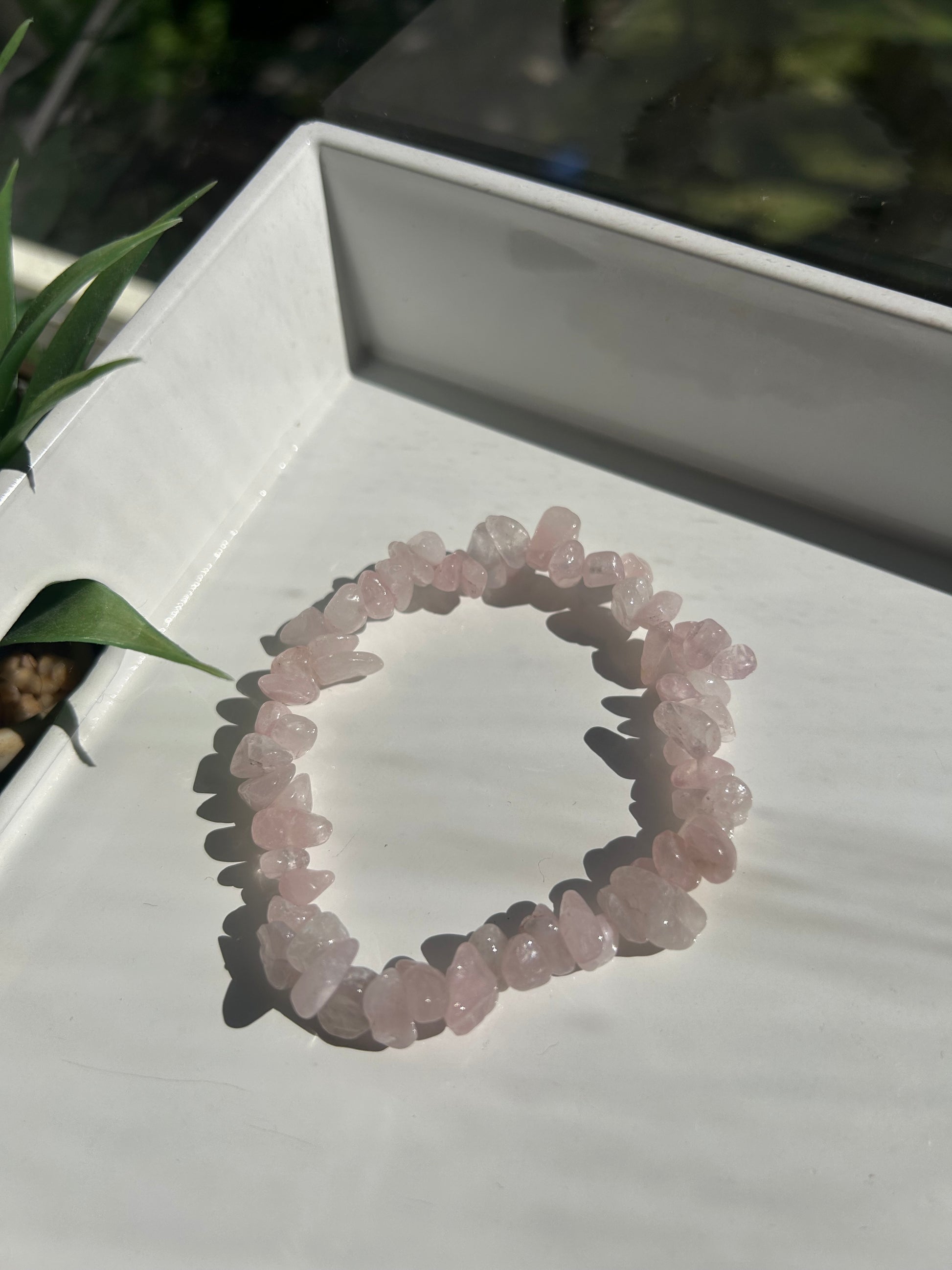 Rose quartz crystal bracelet on a white stand with a blurred natural background