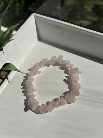 Rose quartz crystal bracelet on a white stand with a blurred natural background
