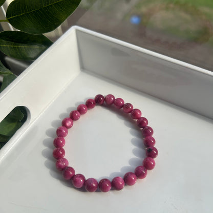 A beaded stretch bracelet made of round magenta-pink beads, resting on a white tray with green leaves in the foreground.
