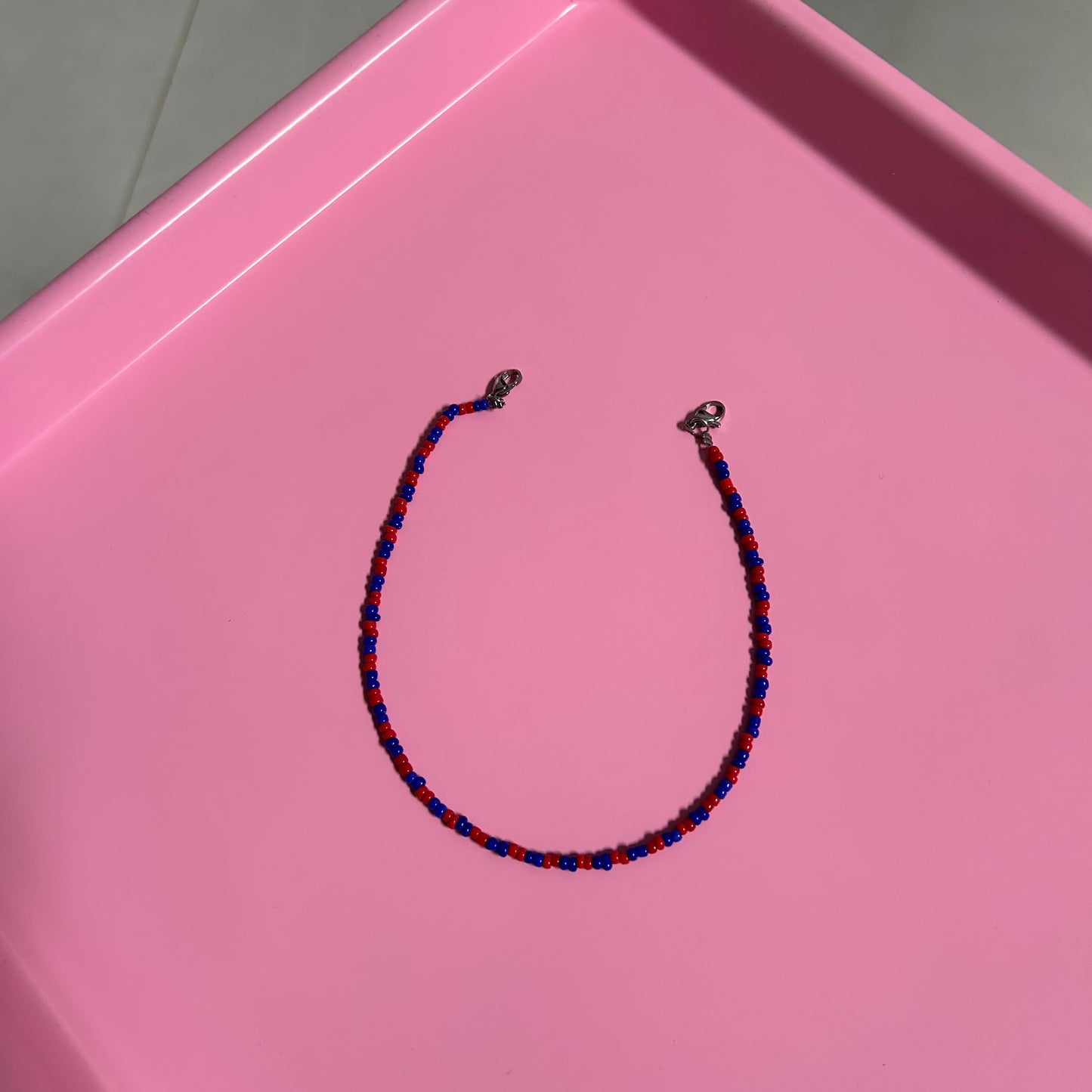 Necklace with blue and red beads on a pink surface