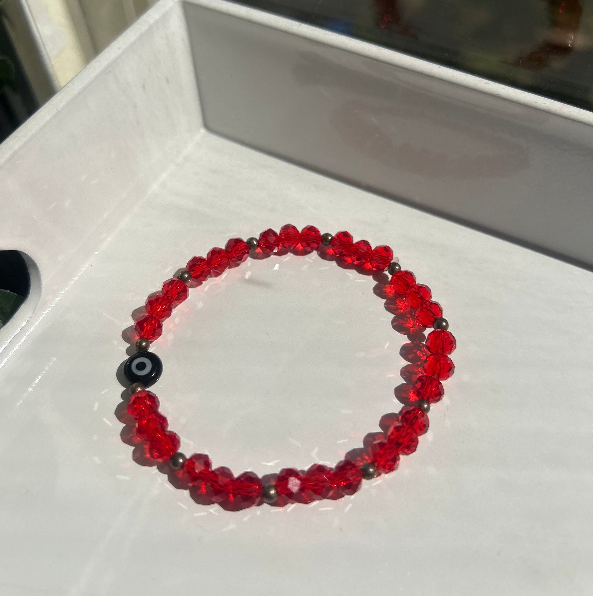 A beaded stretch bracelet made of translucent red faceted beads with a central black evil eye charm, displayed on a white surface.