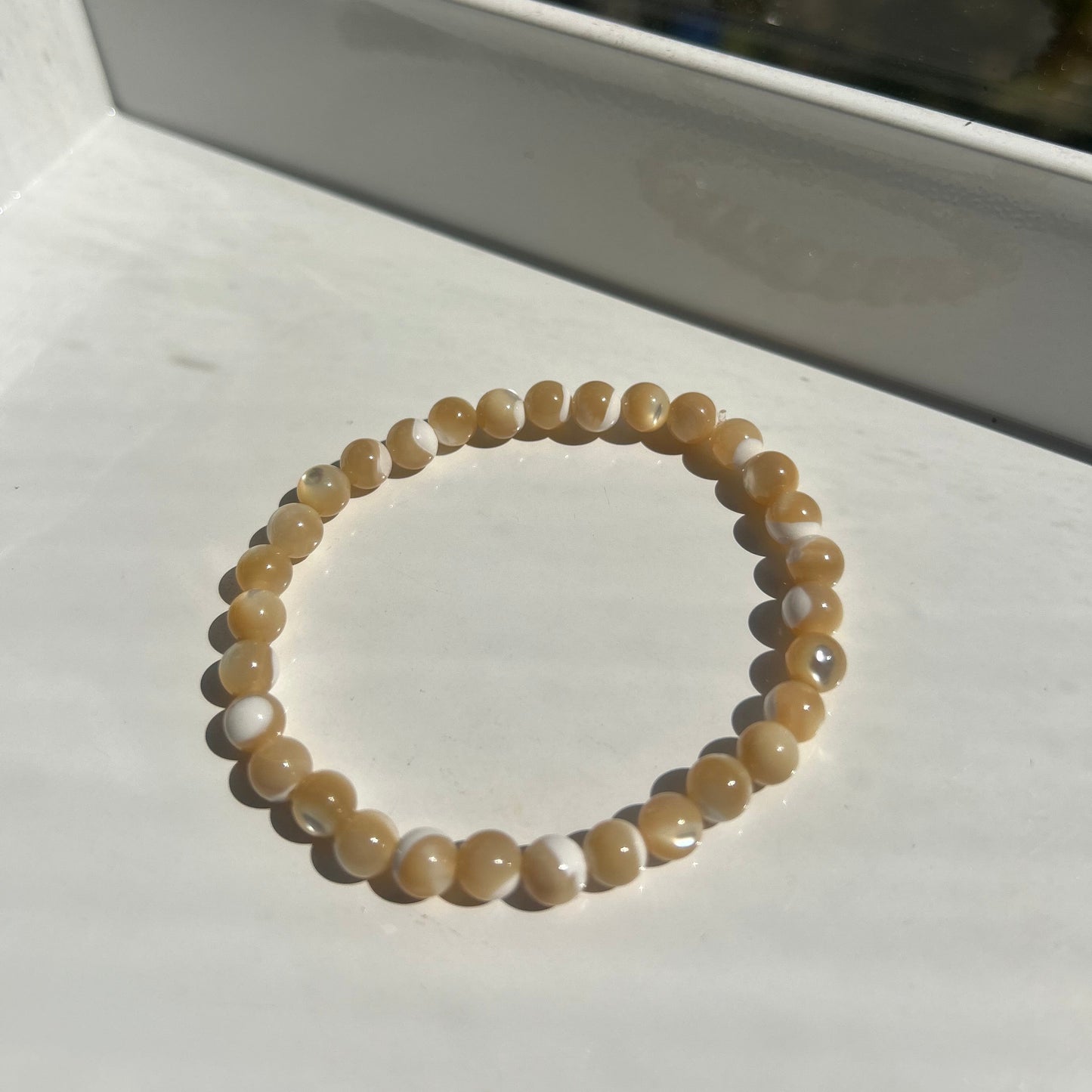 A beaded stretch bracelet made of smooth, round tan and cream beads with subtle white marbling, displayed on a white surface.