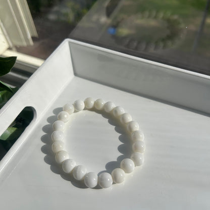 A white beaded bracelet made of smooth, rounded pearls or shell-like beads, displayed on a white tray in bright natural light.