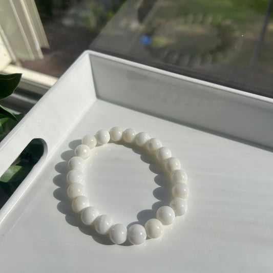 A white beaded bracelet made of smooth, rounded pearls or shell-like beads, displayed on a white tray in bright natural light.